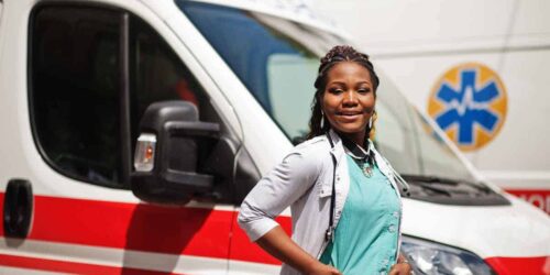 African american female paramedic standing in front of ambulance car.