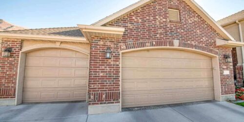 Detached double garage exterior with bricks and concrete driveway. There are two cream colored sectional garage doors complementing the red bricks wall.