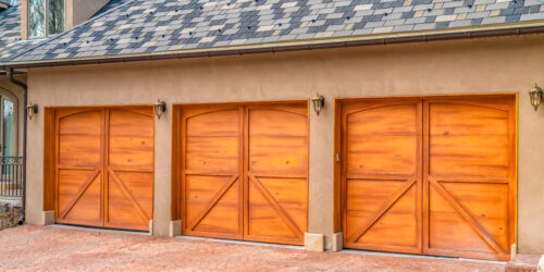 Luxurious exterior of a house with stylish brown wooden garage doors. Vintage lamps are mounted on the concrete wall of the house.
