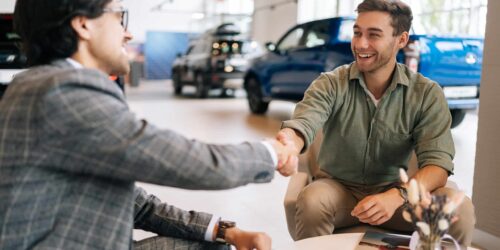 Selective focus of cheerful customer male purchasing automobile in dealership signing paper shaking hands with dealer enjoying successful agreement. Concept of buying new auto at showroom.