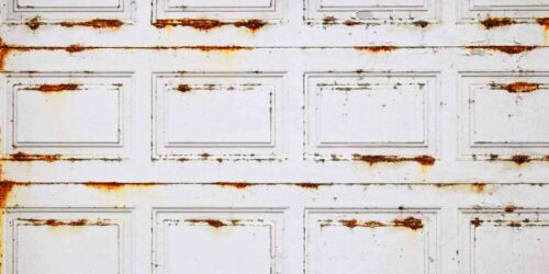 Badly damaged by harsh whether elements metal garage door with rusty spots over white paint, backdrop or background
